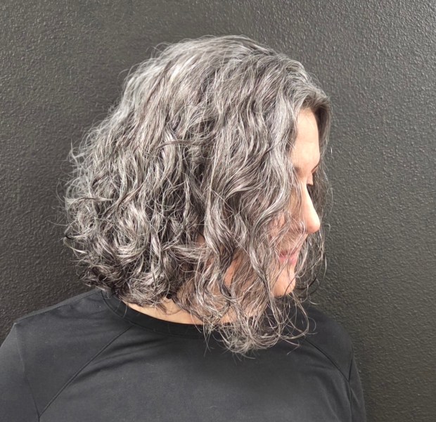 Side profile of a chin-length, curly, A-line haircut on natural silver and grey hair with soft, defined ringlets.