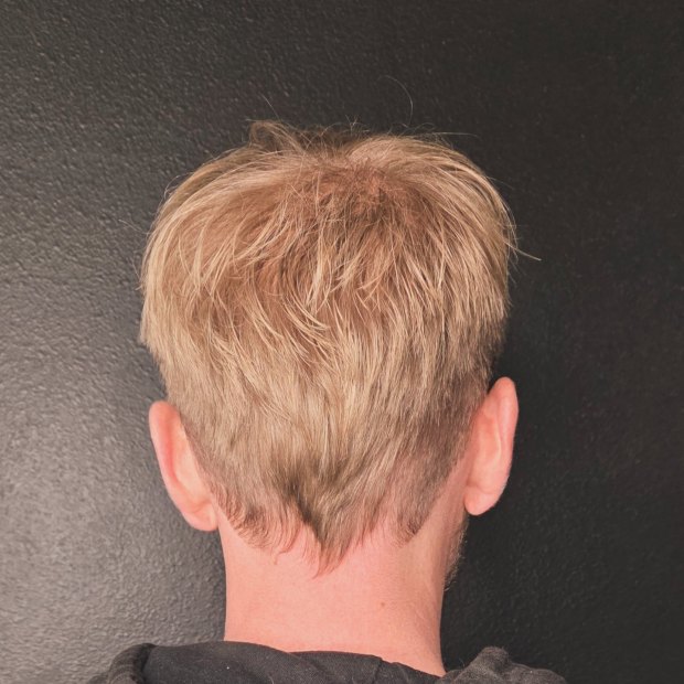 Back view of a short blonde men's cut featuring a natural V-shaped taper at the neckline and short, textured layers on top.