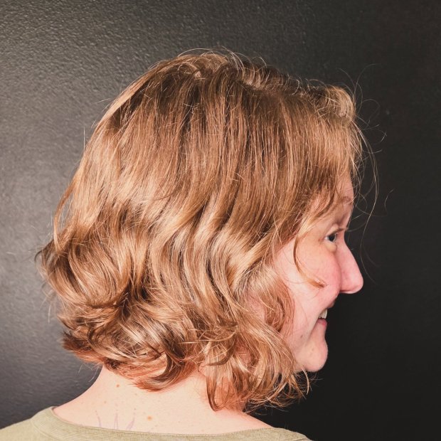 Side profile of a chin-length strawberry blonde bob with soft, tousled waves and layered texture.